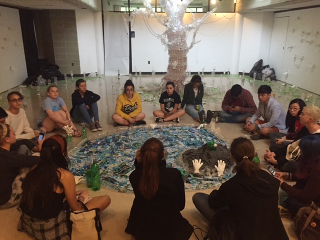Students gather around their installation, "Plastic Park." It's made with water bottles, fabric gloves, and colored elastics. BY ANGIE HILSMAN