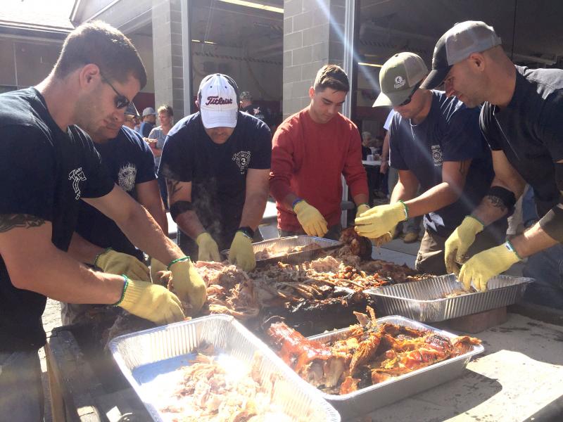 Volunteers pull apart a pig that has just finished cooking. The meat is so tender, it falls apart easily. BY ANGIE HILSMAN