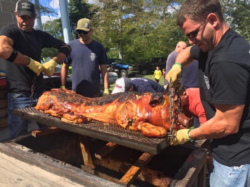 Volunteers hoist the cooked pig out of the box. It originally weighed about 200 pounds, but a lot of it is lost in grease and fat, said Craig Pimental. BY ANGIE HILSMAN
