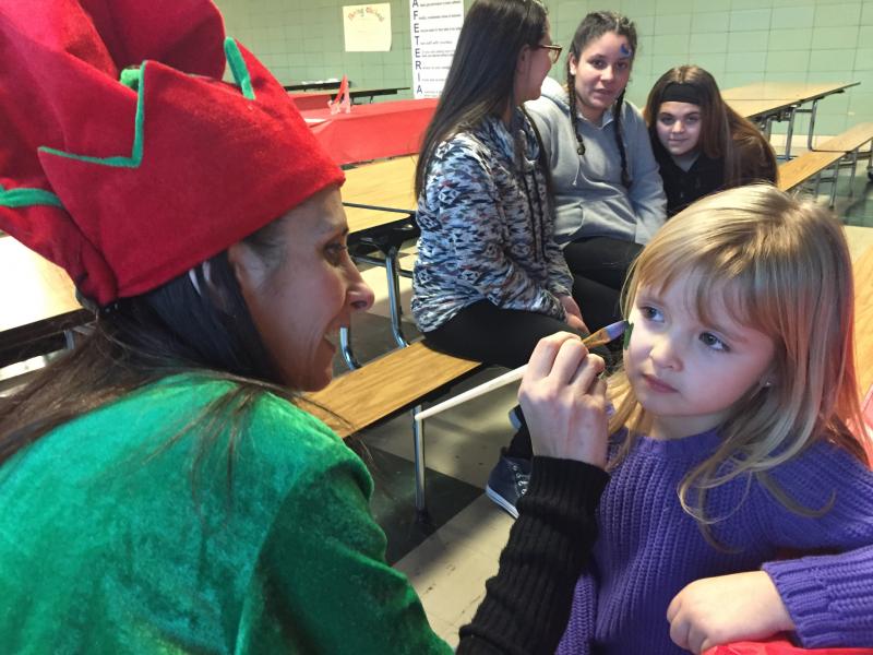 Deborah Medeiros, dressed as an elf, paints Christmas trees on four-year-old Adrianna Antaya's cheeks. BY ANGIE HILSMAN