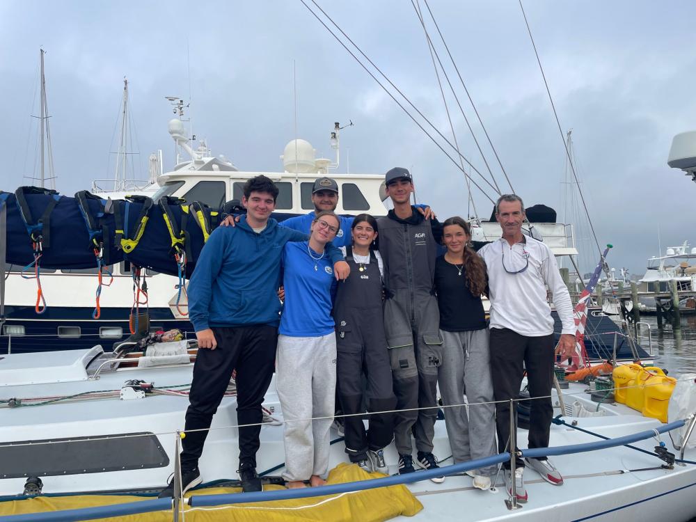 From left to right, Daniel Renehan (Fairhaven, 18), Matthew Prezner (New Bedford, 17), Shealin Palmer (Swansea, 19), Sophie Litos (Dartmouth, 18), Peter Herlihy (Dartmouth, 18), Maisy Sperry (Dartmouth, 18), and Richard Feeny (Bristol, 53). Not pictured are Navigator Tyler Rose (23), Helmswoman Isabella Furey (23), Crew Boss Kevin Tongue (30), and Director at Community Boating Center, Andrew Chin (39). Photo by Brenton Jackson for the New Bedford Light