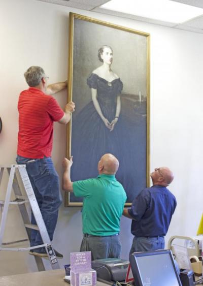 (From left) Bob Glass, Jim Lindell, and Joe Sousa hang one of the refurbished paintings at the Southworth Library. BY NICK WALECKA
