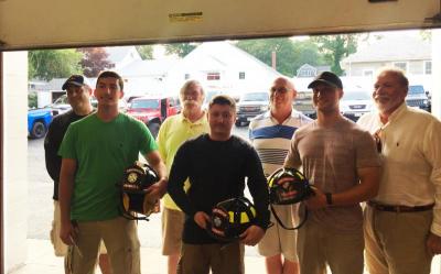 The graduated firefighters show off their new black helmets while the Prudential Committee looks on