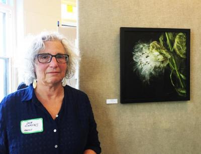 Photographer Deb Ehrens next to her photograph of a milkweed plant carefully lit and layered to mimic a fine art painting