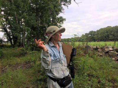 Sommaripa holding a fern at the border of her property, where forest edges on a neighbor’s field.