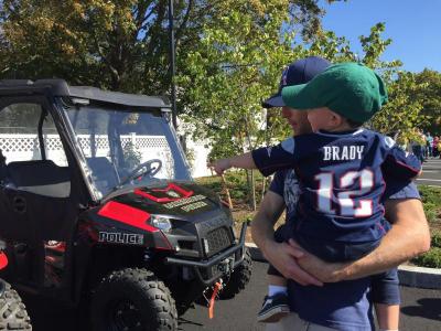 Teddy Taylor, 2, in his Patriots jersey points out his favorite police vehicle to dad Ben while they wait for the station tour.