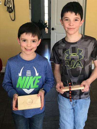 Mason (grade 1) and Spencer (grade 3) Vieira, both Quinn School students, with their inventions: A block to hold a football upright, and a device to weave bracelets. Photo courtesy: Stephanie Vieira