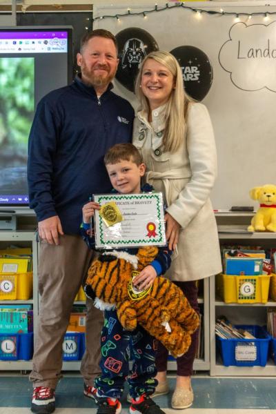 Landon Guile, a six-year-old who recently beat cancer, stands proudly with his parents Jamie (left) and Amy (right) as the Quinn School celebrates “Landon Day” in his honor. Photo by: Morgan Beard.