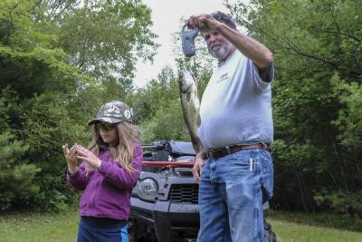 Sage Nicholson, 7, left, wipes off her hands while Donald Goncalez, a tournament volunteer, weighs her catch.
