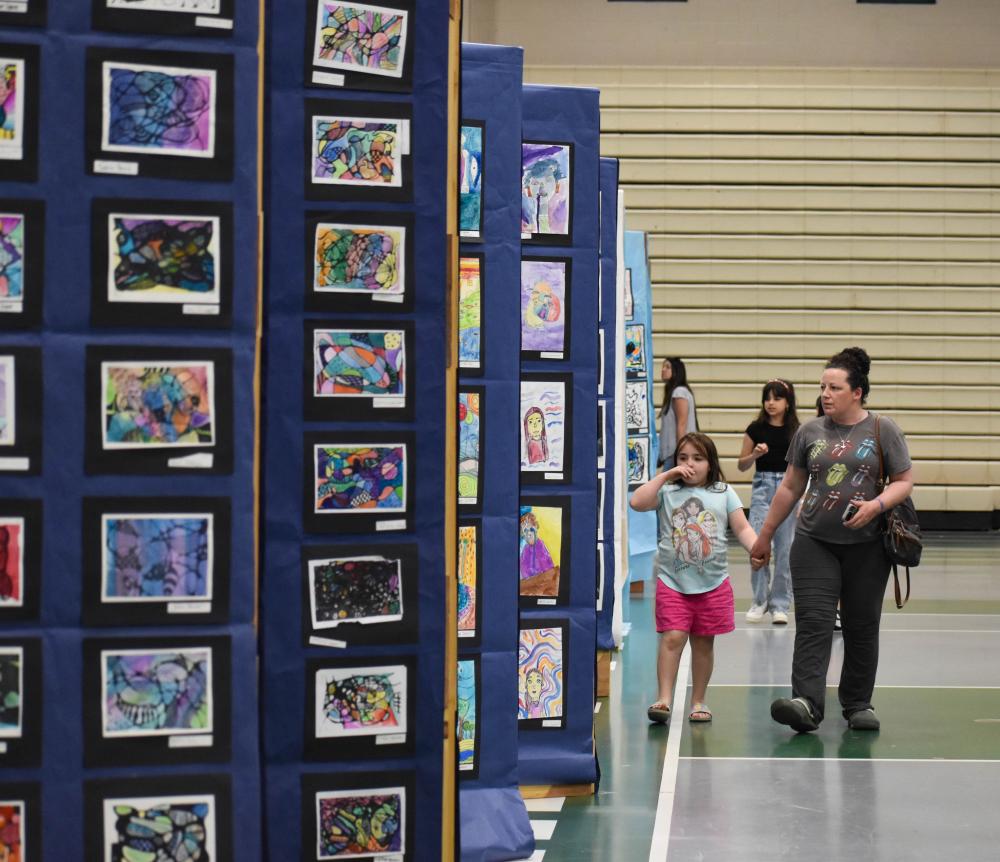 Autumn Roy, 9, and Alicia French walk through the displays of student work.