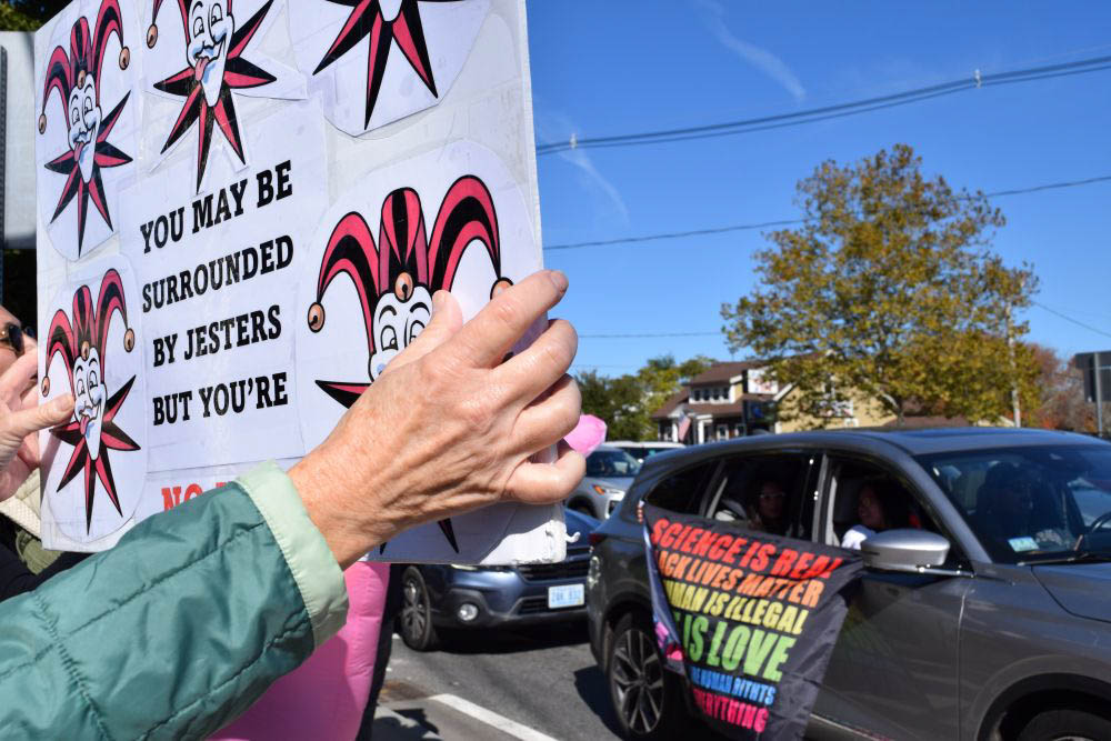 A protester waves her sign to someone driving past with a supportive flag. A protester waves her sign to someone driving past with a supportive flag.
