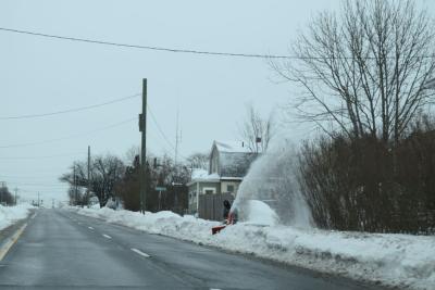 A resident snow-blows the sidewalk.