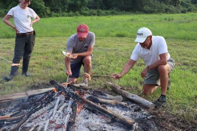 Two men find the best way to roast the hot dogs. 