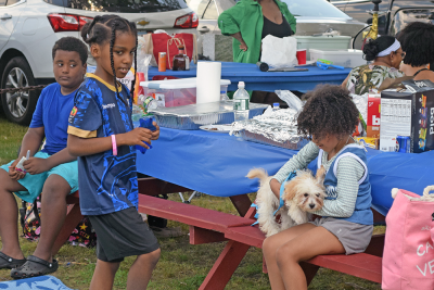 Some kids snuggle with their dog during a BBQ. 
