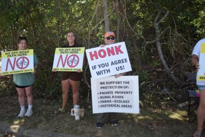 A woman holds a sign explaining why the residents of Old Fall River Road do not support the shared use path. 