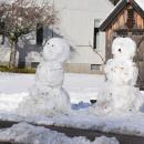 A couple of large snowmen look out at the road.