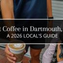 Latte from Scuttlebutt coffee shop in Padanaram Village, Dartmouth, MA, held outside the storefront with a bouquet of flowers and a black dog