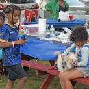 Some kids snuggle with their dog during a BBQ. 