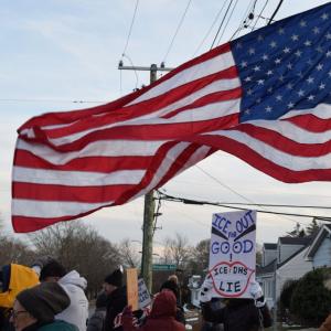 An American flag waves over a sign against I.C.E. Photos by Kat Sheridan