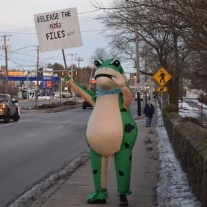 A frog holds a pun sign calling for the publication of the Epstein files.