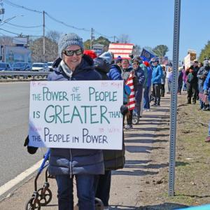 A protester holds a sign stating people are more powerful as a group.