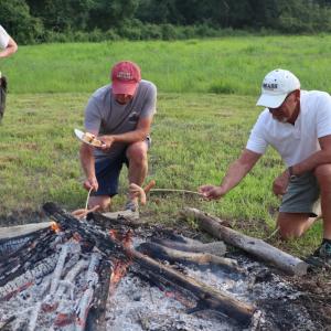 Two men find the best way to roast the hot dogs. 
