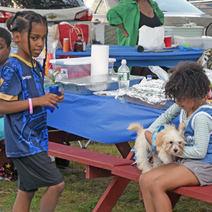 Some kids snuggle with their dog during a BBQ. 