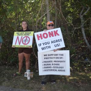 A woman holds a sign explaining why the residents of Old Fall River Road do not support the shared use path. 