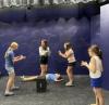 Five young women act out a scene on stage in a class